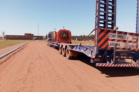 Prancha carregada com peça industrial de grande porte, atravessando o pátio de uma unidade industrial.
