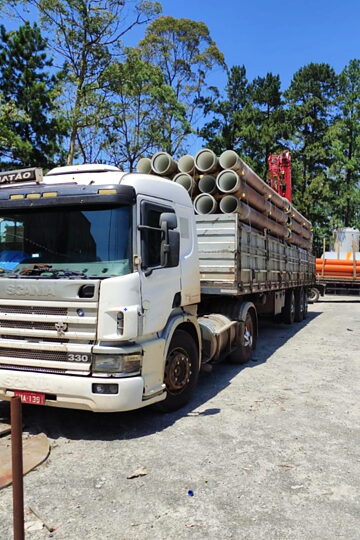 Carreta carregada com tubos de concreto de grande diâmetro, pronta para o transporte.
