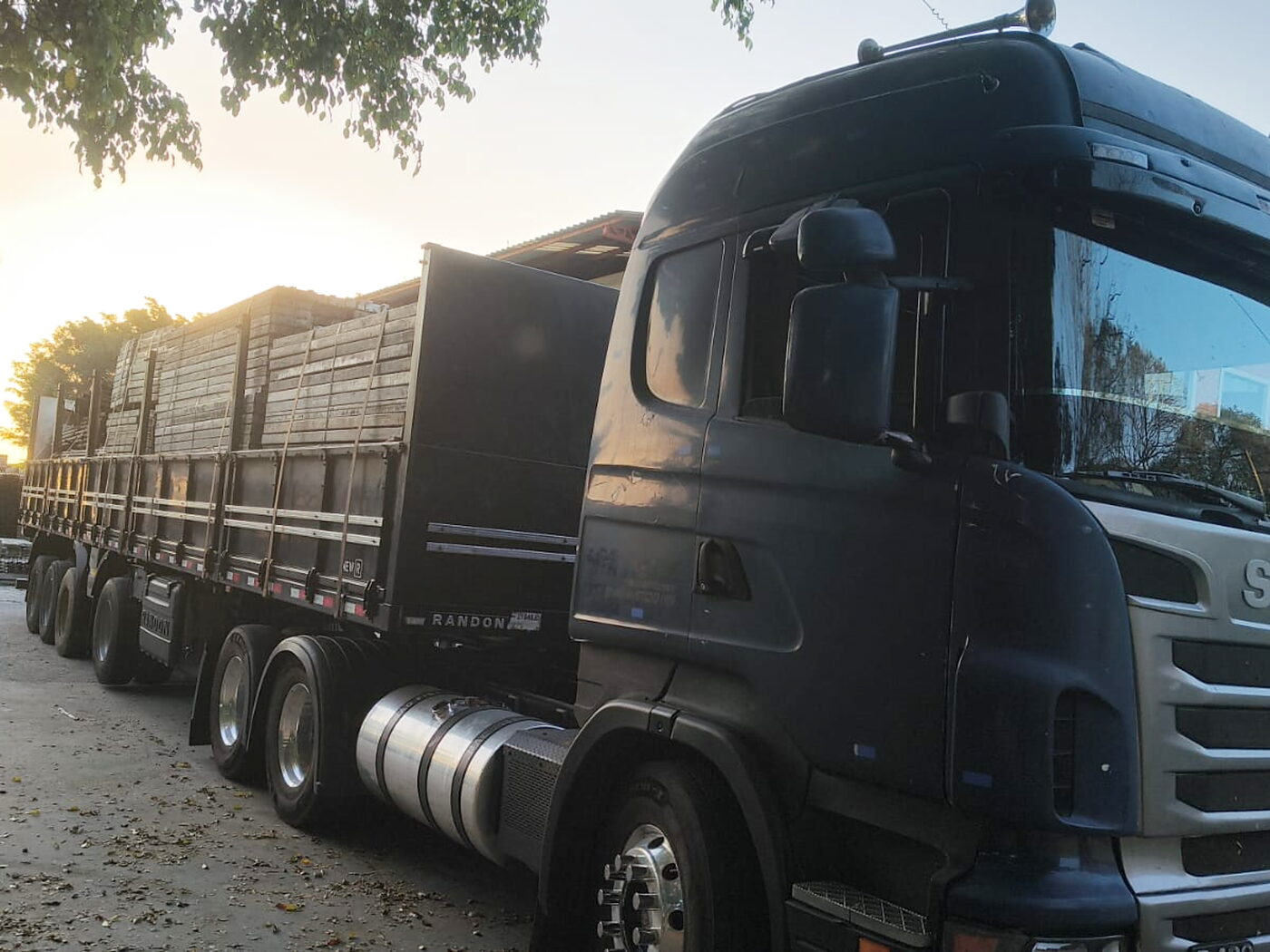 Cavalo mecânico engatado à carreta carregada, pronto para sair, com o sol se pondo ao fundo.
